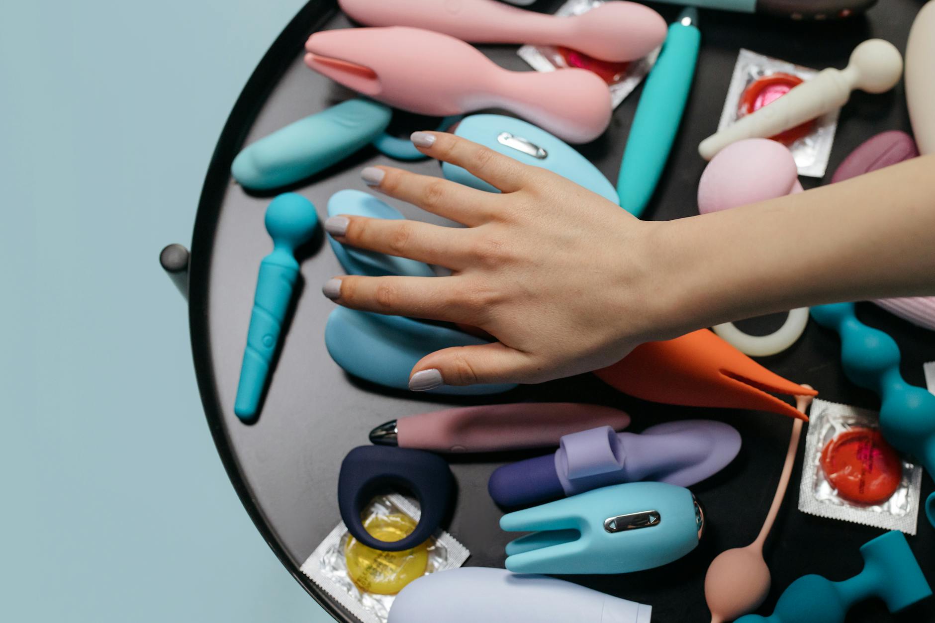 Hands exploring colorful intimate wellness toys on a neutral surface