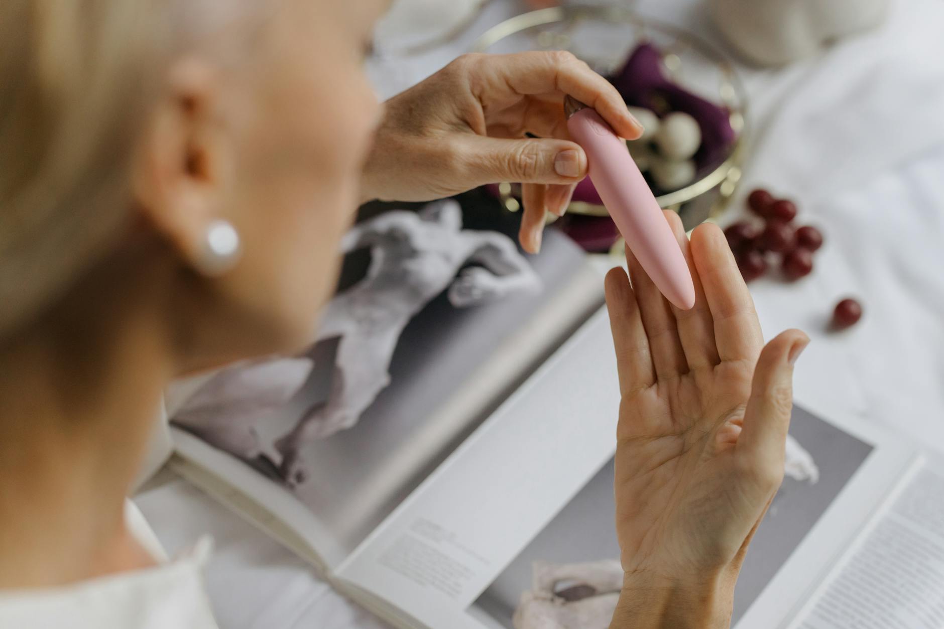 Close-up of a hand holding a pink vibrator with art books in soft background, symbolizing personal healing and intimate reconnection