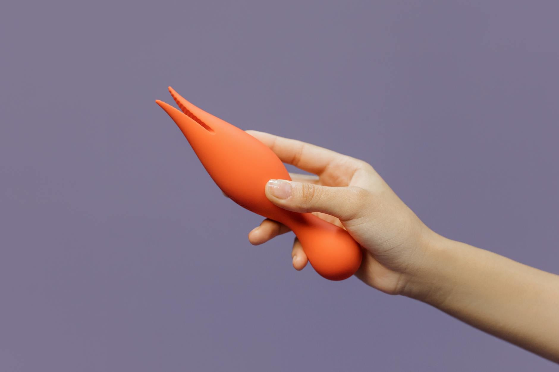 Hand holding a lemon-shaped vibrator against a minimalistic purple backdrop, showcasing modern sensuality